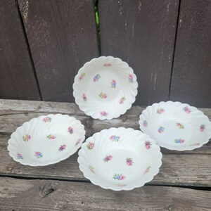 May include: Four white ceramic bowls with scalloped edges and a floral pattern in pink, blue, and yellow.