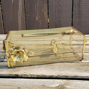 May include: Gold metal tissue box cover with a floral design. The cover is made of wire mesh and has a rectangular shape.