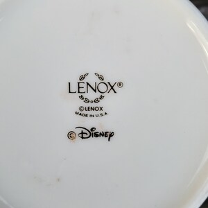 May include: Close-up of the bottom of a white ceramic mug with black text that reads "LENOX&reg;", "&copy;LENOX MADE IN U.S.A." and "&copy;DISNEY".