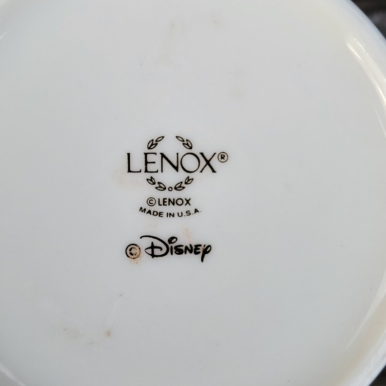 May include: Close-up of the bottom of a white ceramic mug with black text that reads "LENOX&reg;", "&copy;LENOX MADE IN U.S.A." and "&copy;DISNEY".