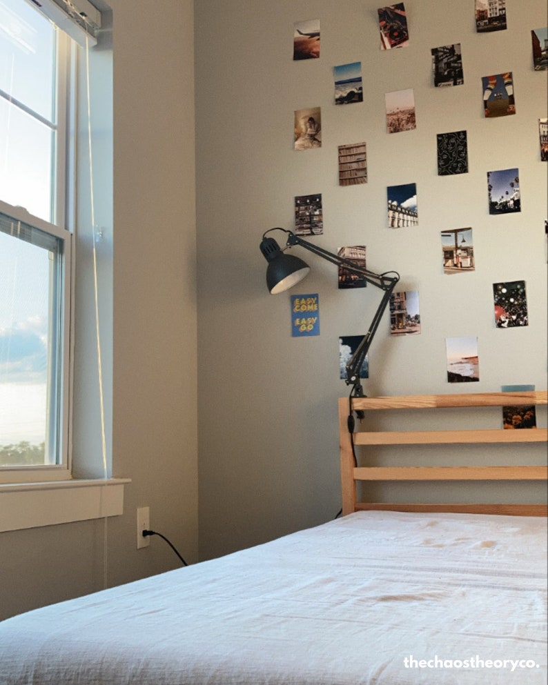 May include: A white bed with a wooden headboard and a black desk lamp with a flexible arm. The wall behind the bed is decorated with a collage of photos.