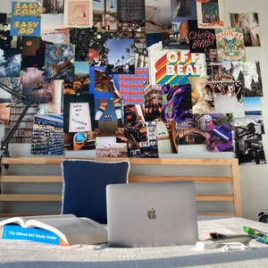May include: A collage of images and text on a wall above a bed with a laptop, a book, and a white pillow. The collage includes images of palm trees, a beach, a city, and a person on a surfboard. The text includes the words "Easy Come Easy Go", "Hi-Five", "Self Cheers", "Off Beat", "Weekend", and "Cherry Bomb".