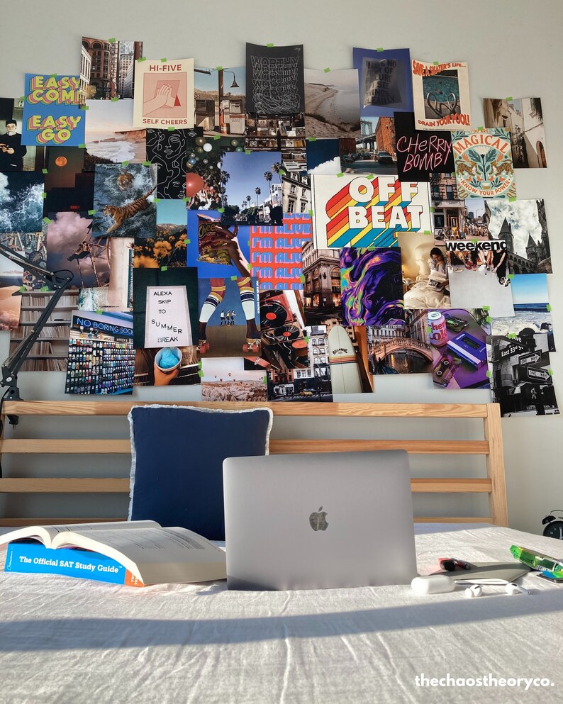 May include: A collage of images and text on a wall above a bed with a laptop, a book, and a white pillow. The collage includes images of palm trees, a beach, a city, and a person on a surfboard. The text includes the words "Easy Come Easy Go", "Hi-Five", "Self Cheers", "Off Beat", "Weekend", and "Cherry Bomb".