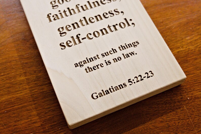 May include: A rectangular wooden plaque with engraved text. The text includes the words "goodness, faithfulness, gentleness, self-control" and a Bible verse reference. The plaque is light-colored.