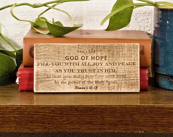 Letrero rústico de madera con versículo bíblico grabado de Romanos 15:13, ideal como regalo para el hogar.