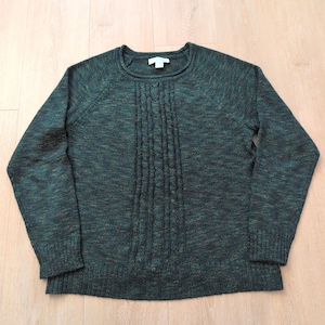 May include: A dark green long-sleeve sweater featuring a speckled, multi-colored knit texture and a vertical cable knit pattern down the center front. The garment has a round neckline, ribbed cuffs, and a ribbed hemline for a finished look.