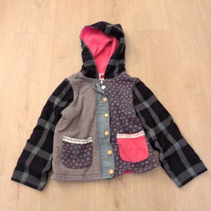 May include: A hooded jacket featuring a black and gray plaid pattern on the sleeves and hood, with a bright pink hood lining. The front panels are mismatched with gray fabric and a floral print, including two pockets with lace trim and gold buttons.