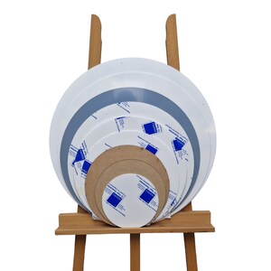 K&ouml;nnte beinhalten: Eine Sammlung runder Perspex-Platten in verschiedenen Gr&ouml;&szlig;en, pr&auml;sentiert auf einer h&ouml;lzernen Staffelei. Die Platten sind wei&szlig;, grau und braun, einige mit Schutzfolie und Text mit der Aufschrift "PERSPEX" und "10 Year Guarantee".