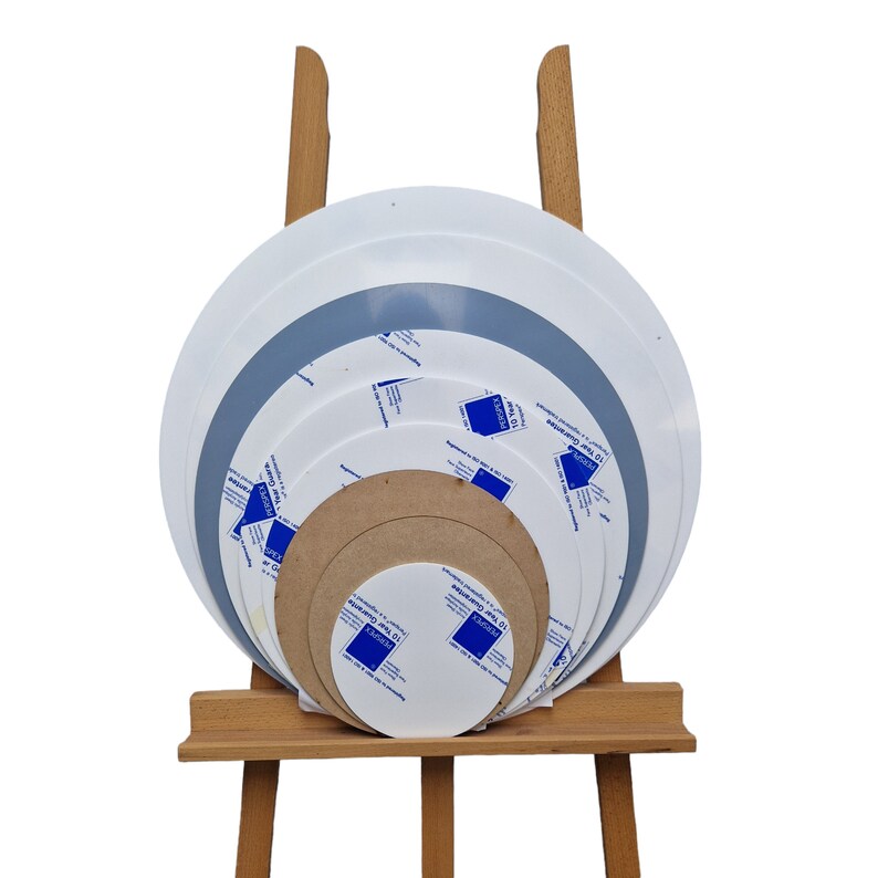 K&ouml;nnte beinhalten: Eine Sammlung runder Perspex-Platten in verschiedenen Gr&ouml;&szlig;en, pr&auml;sentiert auf einer h&ouml;lzernen Staffelei. Die Platten sind wei&szlig;, grau und braun, einige mit Schutzfolie und Text mit der Aufschrift "PERSPEX" und "10 Year Guarantee".