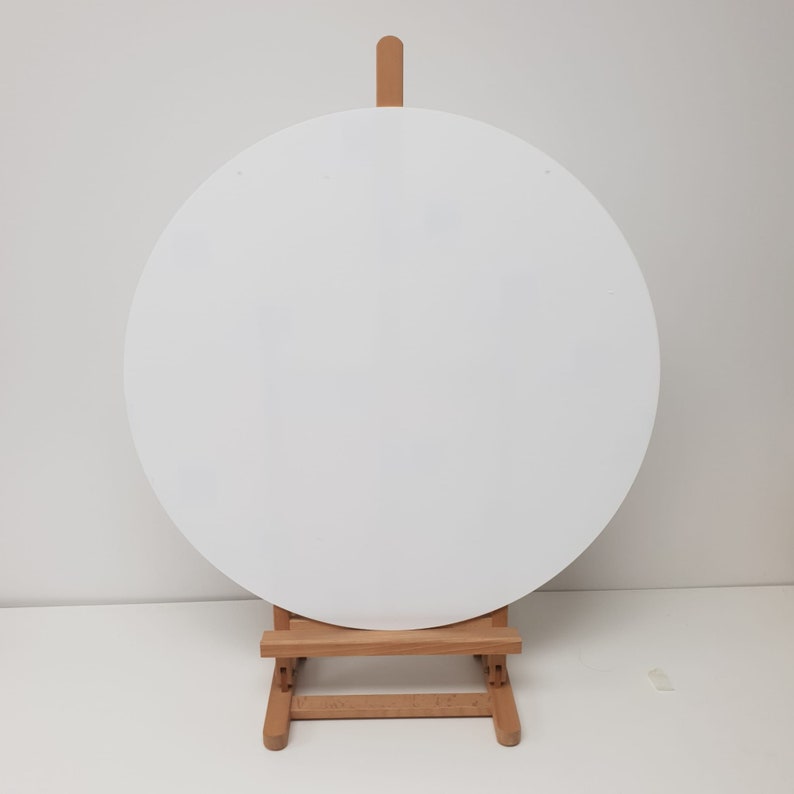K&ouml;nnte beinhalten: Eine wei&szlig;e, runde Leinwand steht auf einer kleinen Holzstaffelei. Die Staffelei besteht aus hellem Holz und hat ein einfaches, faltbares Design. Die leere Leinwand bietet eine saubere, minimalistische &Auml;sthetik, perfekt zum Malen oder Pr&auml;sentieren von Kunstwerken.