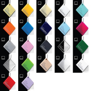 K&ouml;nnte beinhalten: Eine Sammlung von Perspex-Farbmustern, jeweils an einer silbernen Kette befestigt. Die Muster sind quadratisch und in einer Vielzahl von Farben erh&auml;ltlich, darunter Gelb, Orange, Blau, Rosa, Grau, Gr&uuml;n und Rot. Auf jedem Muster steht das Wort "PERSPEX".
