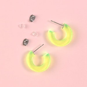 May include: A pair of neon green hoop earrings with silver posts on a pink background.