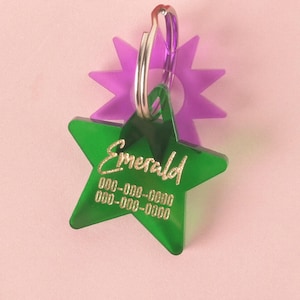 May include: Green star-shaped pet ID tag with the word "Emerald" and phone numbers in gold lettering. The tag is attached to a purple star-shaped charm.