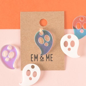 May include: Four iridescent ghost-shaped ornaments with cut-out eyes. The ornaments are on a light pink and orange background. The text "EM & ME" is printed on a brown card.