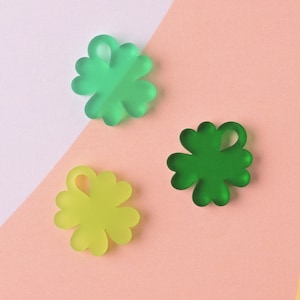 Op de afbeelding: Drie klavertjesvier-charms in groen en geel. De charms zijn gemaakt van acryl en hebben een glanzende afwerking.