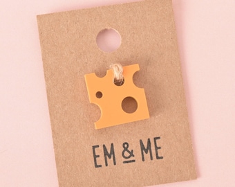 May include: A small orange cheese charm with holes, hanging from a brown tag with the text "EM & ME" printed on it.