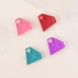 May include: Four diamond-shaped charms in different colours: pink, red, purple, and blue. Each charm has a small hole at the top.
