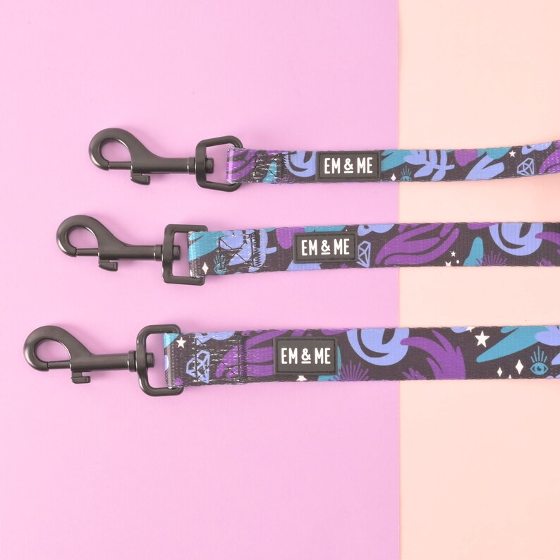 May include: Three black dog leashes with purple, blue, and white abstract patterns. Each leash has a black metal clip and a black label with the text "EM & ME" printed in white.