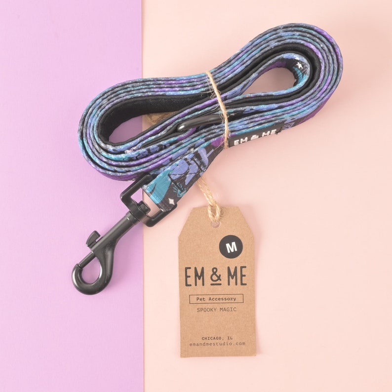 May include: A purple and blue patterned dog leash with a black metal clip and a brown tag that says "EM & ME Pet Accessory SPOOKY MAGIC CHICAGO, IL em&mestudio.com" and "M".