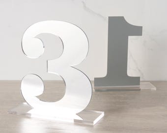 Números de mesa prateados em fonte clássica Clarendon para decoração de recepções de casamento e eventos.