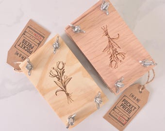 May include: Two wooden flower presses with engraved floral designs. The presses are made of pine and oak and have metal clamps. The smaller press is 3" x 4" and the larger press is 4" x 5".
