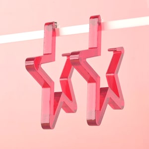 Könnte beinhalten: Ein Paar rote sternförmige Ohrringe. Die Ohrringe sind aus Acryl und haben eine glänzende Oberfläche.