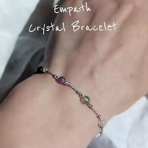 Könnte beinhalten: Ein zartes silberfarbenes Kettenarmband mit kleinen, polierten, mehrfarbigen Edelsteinperlen in Violett, Grün und Transparent, mit dem in weißer Schreibschrift überlagerten Text Empath Crystal Bracelet.