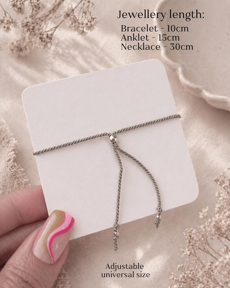 Puede incluir: Una pulsera de cord&oacute;n gris con cierre de cuenta met&aacute;lica deslizante sobre una tarjeta blanca. El texto dice: Jewellery length: Bracelet - 10cm, Anklet - 15cm, Necklace - 30cm. Abajo, el texto dice: Adjustable universal size.