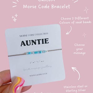 Könnte beinhalten: Ein individuelles Morsecode-Armband mit dem Wort "AUNTIE" auf einer Karte. Das Armband hat hellblaue Saatperlen. Auf der Karte steht auch "Secret message jewellery" und "WWW.LAGEM.CO.UK". Das Armband hat eine Edelstahl- oder Sterlingsilber-Oberfläche.
