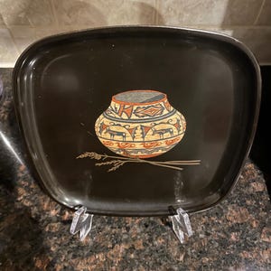 May include: A black square tray with a raised rim features a stylized image of a Native American pottery vessel with geometric patterns in red, orange, and black. The vessel is surrounded by stylized grass.