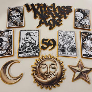 May include: A selection of decorative items with a celestial and mystical theme. Includes tarot card designs with skulls, moons, and suns, along with a crescent moon, star, and the text "Witches Never Age" and the number "59".