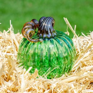 May include: A green glass pumpkin with brown swirl details sits on a bed of straw.