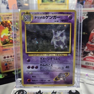 Puede incluir: Una carta coleccionable Pok&eacute;mon japonesa con Gengar, un personaje p&uacute;rpura de tipo fantasma. La carta est&aacute; en una funda protectora y tiene texto japon&eacute;s. El dise&ntilde;o de la carta incluye una ilustraci&oacute;n de Gengar sonriente, HP80 y otros detalles.