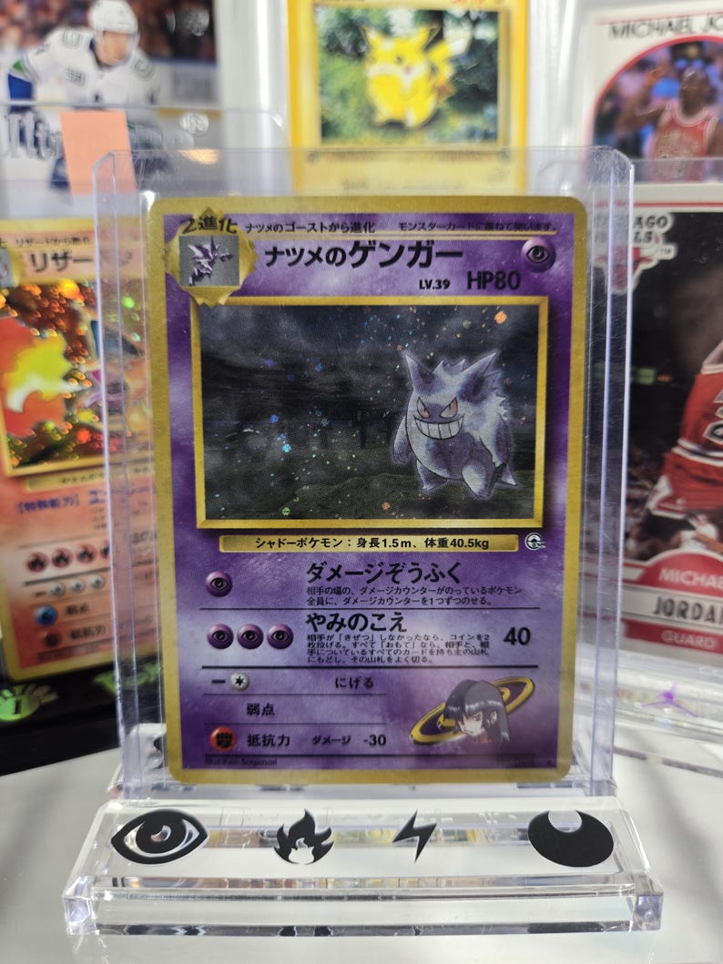 Puede incluir: Una carta coleccionable Pok&eacute;mon japonesa con Gengar, un personaje p&uacute;rpura de tipo fantasma. La carta est&aacute; en una funda protectora y tiene texto japon&eacute;s. El dise&ntilde;o de la carta incluye una ilustraci&oacute;n de Gengar sonriente, HP80 y otros detalles.