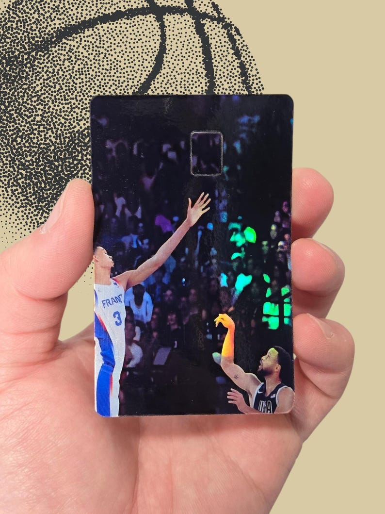 May include: A rectangular black card featuring a basketball player in a blue, white, and red uniform, reaching for the ball. The card has a glossy finish and a basketball design in the background.