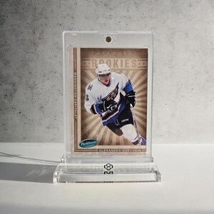 Puede incluir: Una tarjeta de hockey con Alexander Ovechkin con el uniforme de los Washington Capitals, exhibida en un soporte y expositor de acr&iacute;lico transparente. La tarjeta tiene el texto "Parkhurst Rookies" y "Washington Capitals".