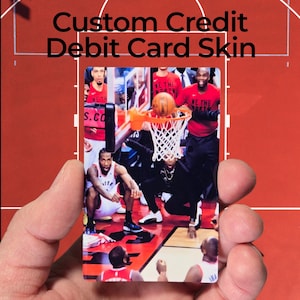 May include: A custom credit/debit card skin featuring a basketball court scene with players in action. The card has the text "Custom Credit Debit Card Skin" in black. The card is held in a hand.