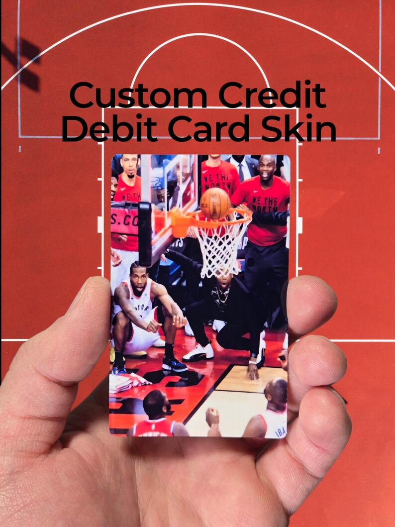 May include: A custom credit/debit card skin featuring a basketball court scene with players in action. The card has the text "Custom Credit Debit Card Skin" in black. The card is held in a hand.