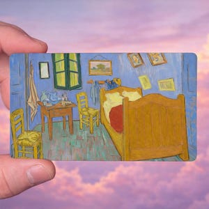 May include: A miniature rectangular painting of Van Gogh's "Bedroom in Arles" held against a pink and purple sky. The artwork depicts a yellow bed, chairs, and table in a blue room with framed pictures.