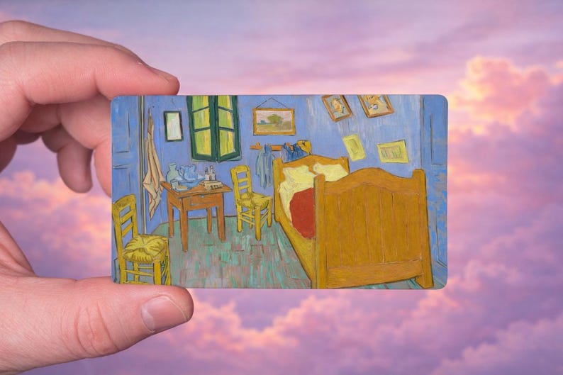 May include: A miniature rectangular painting of Van Gogh's "Bedroom in Arles" held against a pink and purple sky. The artwork depicts a yellow bed, chairs, and table in a blue room with framed pictures.