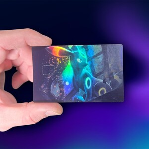May include: A holographic trading card featuring a stylized illustration of a dark-colored creature with glowing accents. The card has a rectangular shape and is held against a dark blue and purple gradient background.