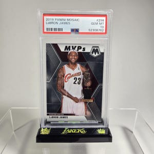 Puede incluir: Una tarjeta de baloncesto LeBron James 2019 Panini Mosaic, calificada GEM MT 10, en una funda protectora. La tarjeta presenta a LeBron James con el uniforme de los Cavaliers de Cleveland sosteniendo un trofeo. La tarjeta est&aacute; sobre un soporte negro con texto "King James" y "Lakers".