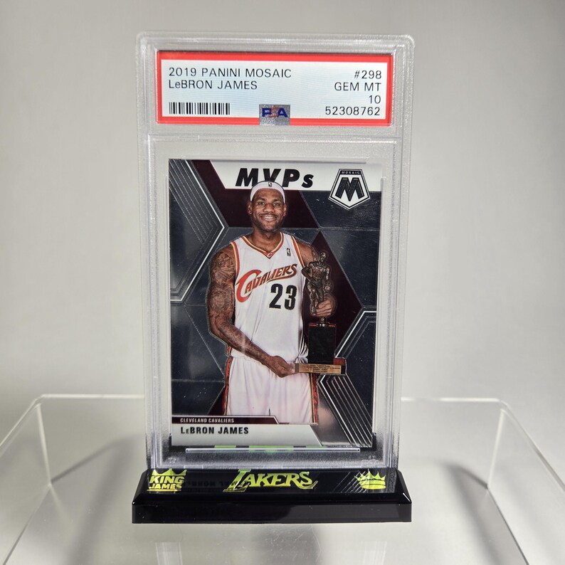 Puede incluir: Una tarjeta de baloncesto LeBron James 2019 Panini Mosaic, calificada GEM MT 10, en una funda protectora. La tarjeta presenta a LeBron James con el uniforme de los Cavaliers de Cleveland sosteniendo un trofeo. La tarjeta est&aacute; sobre un soporte negro con texto "King James" y "Lakers".