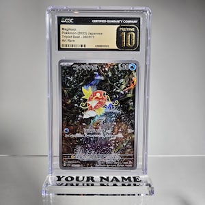 Puede incluir: Una carta de Pok&eacute;mon Magikarp calificada en una funda protectora transparente. La carta presenta una colorida ilustraci&oacute;n de una criatura con forma de pez con el texto "Magikarp" y "Triplet Beat - 080/073". La funda est&aacute; etiquetada como "PRISTINE 10".