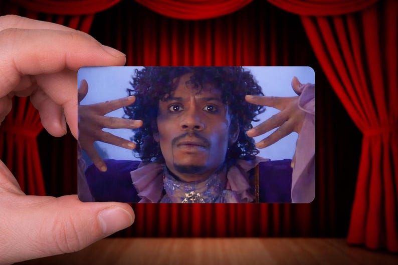 May include: A rectangular card featuring a person with curly hair, wearing a purple outfit with a ruffled collar. The person is making a hand gesture. The background is a red curtain.
