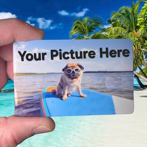 May include: A rectangular card with the text "Your Picture Here" in black. The card features an image of a pug wearing sunglasses on a blue paddleboard in the ocean. The background shows a beach scene with palm trees and a blue sky.