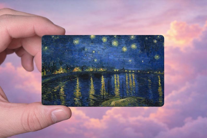 May include: A rectangular card featuring a painting of a night scene with a river reflecting lights and stars. The artwork is dominated by dark blues and yellows, reminiscent of Van Gogh's style. The card is held against a backdrop of a pink and purple sky.