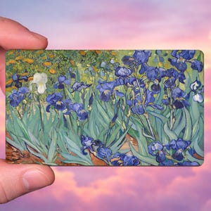May include: A rectangular art print featuring a painting of blue irises in a field. The artwork has a vibrant color palette with shades of blue, green, yellow, and brown. The print is held against a backdrop of a pink and purple sky.
