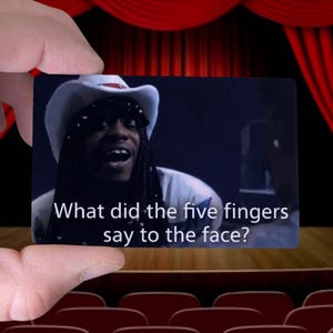 May include: A rectangular card held by a hand displays a scene with a person wearing a cowboy hat. The text on the card reads, "What did the five fingers say to the face?" The background features a stage with red curtains and theater seating.