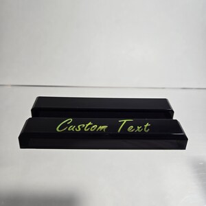 Puede incluir: Dos organizadores de escritorio rectangulares negros con bordes biselados. El organizador frontal tiene las palabras "Custom Text" en una fuente verde brillante, escrita a mano. Los organizadores est&aacute;n sobre una superficie reflectante.